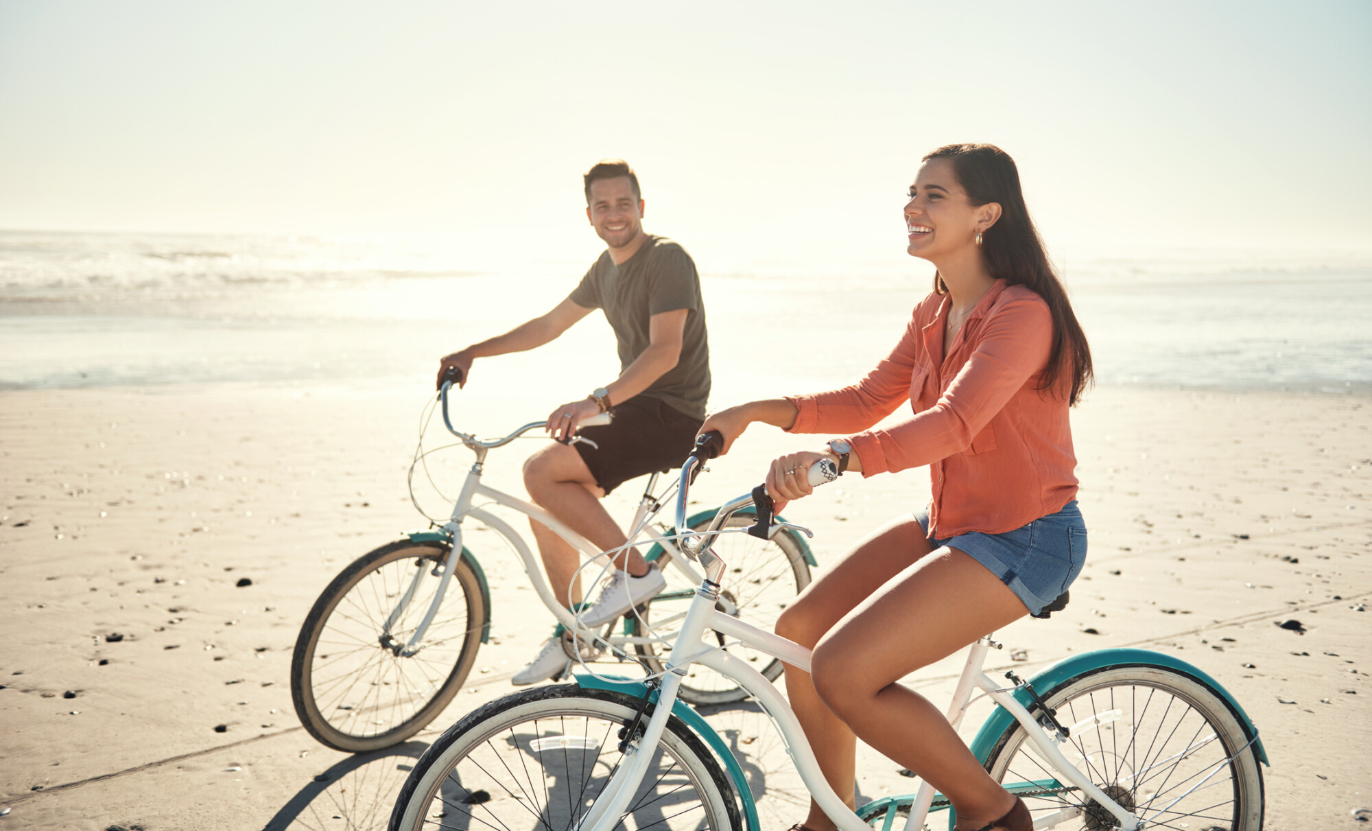 Young caucasian couple enjoying riding bicycles on holiday at the beach
